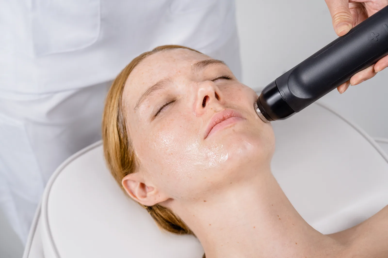 Glo2Facial handpiece gliding over a client's cheek during an oxygen facial treatment